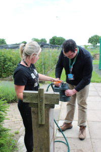 A member of staff from the Lifeskills faculty at Activate Learning helps Dylan fill his watering can. 