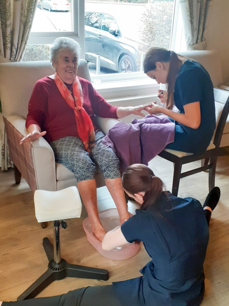 Two beauty therapy students giving beauty treatments to an elderly lady in independent living